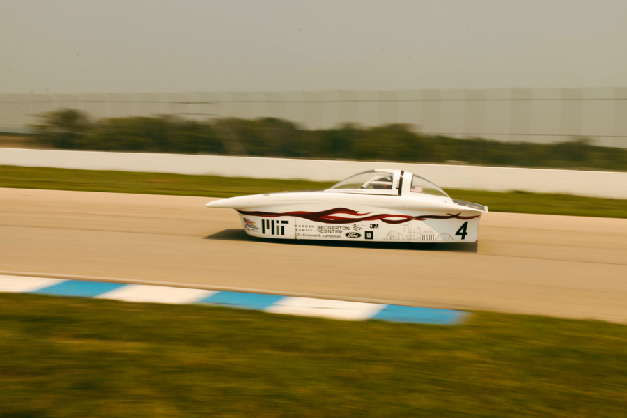 MIT's solar car is seen zooming down a racetrack, with everything but the car slightly blurred