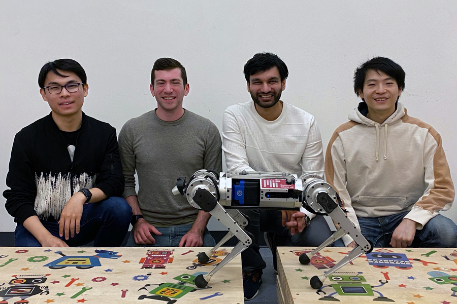 Four MIT researchers pose, smiling, behind the mini cheetah robot