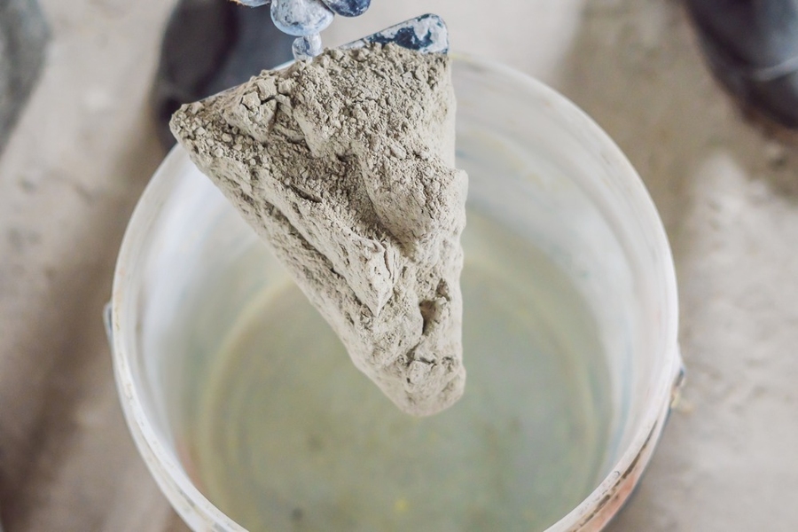 Close-up photo of a trowel with a cement mixture above a blurred-out bucket containing liquid