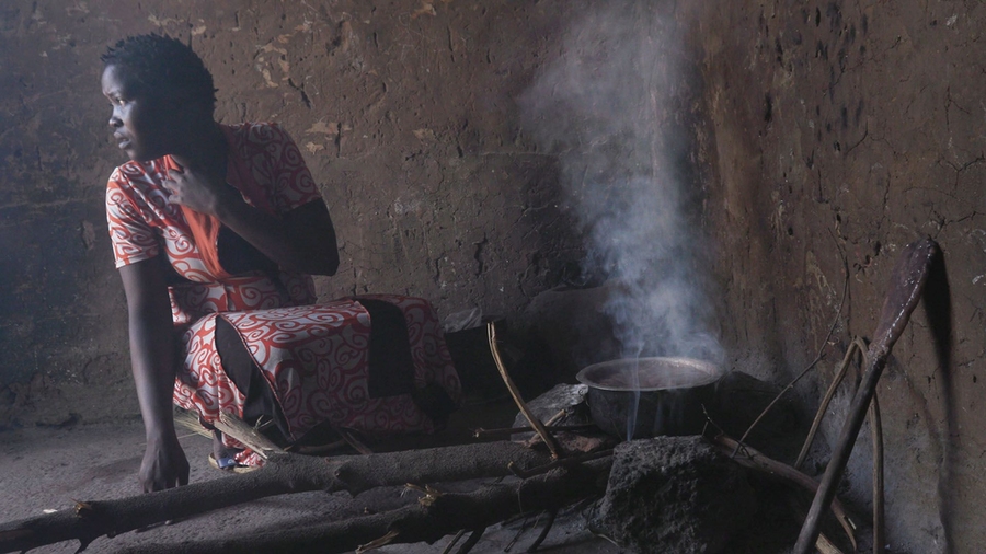 Photo of a woman from Uganda looking off into the distance as she uses her cookstove.