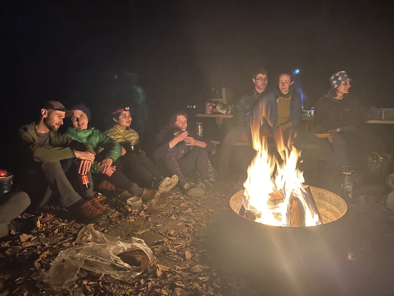 Photo of MIT Outing Club members relaxing around a campfire at night.