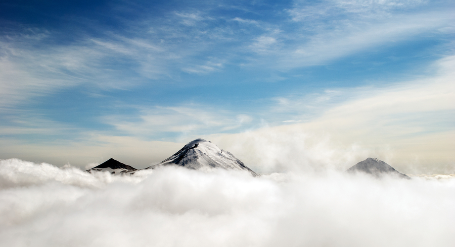 Photo of three mountain peaks above some clouds