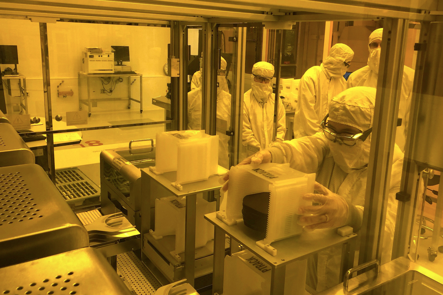 Photo of five or six students in clean suits in the MIT.nano clean room. The entire image has a yellow-orange tint.