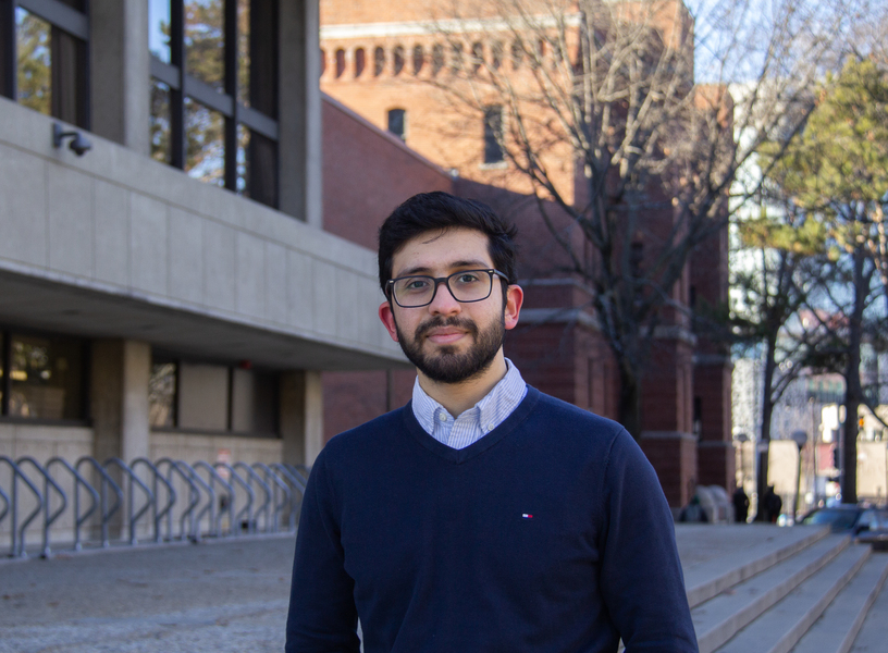 Photo of Meshkat Botshekan standing outdoors with an MIT building and a couple of trees in the background