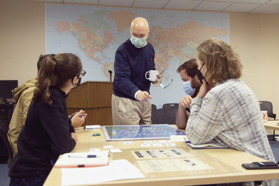 Photo of Eric Heginbotham, masked, standing at a table with MIT students sitting around it