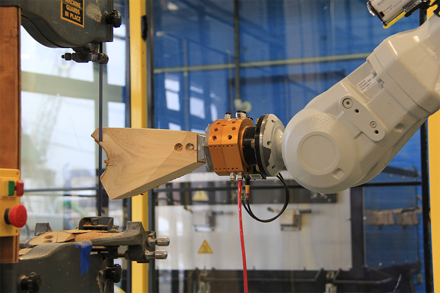 Photo of a robotic arm pushing a tree fork through a band saw. 