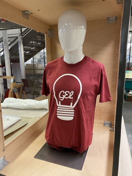 Photo of a manequin torso wearing a red GEL T-shirt in an open wooden box