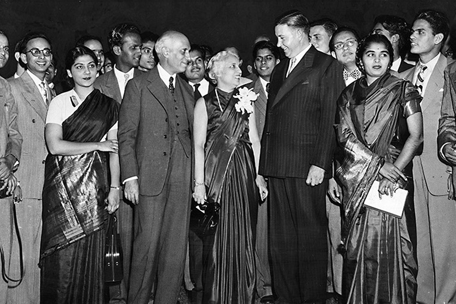 Black-and-white photo of Prime Minister Jawaharlal Nehur standing along with about two dozen people, all wearing either suits and ties or traditional Indian dresses