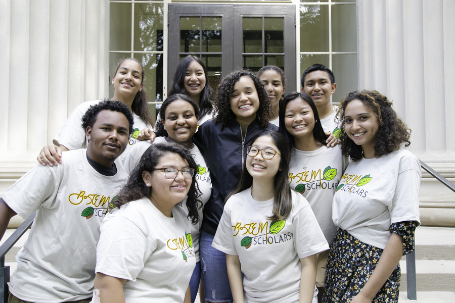 11 smiling people gather for a group photo on steps of the MIT campus