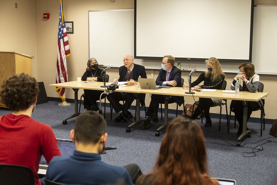 Five presenters seated at a table in front of an audience gathered in a classroom.