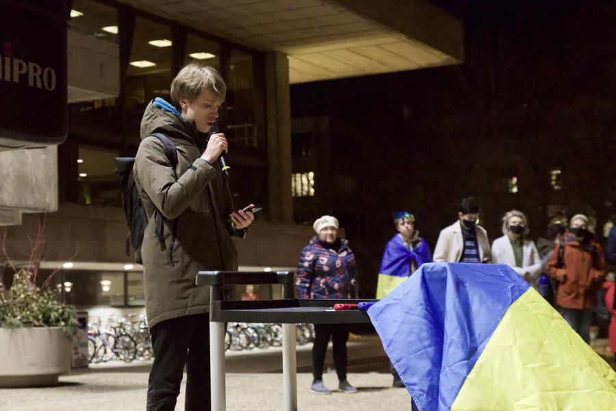 Artem Laptiev speaks at Ukrainian rally. A blue-and-yellow Ukrainian flag is seen at right.