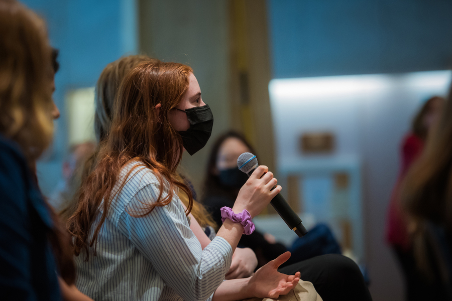 Side view of a student, seated and wearing a face mask, asking a question during a Q&A session