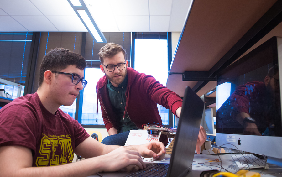 Lecturer Joe Steinmeyer leans over a student's keyboard to point to a section of computer monitor.
