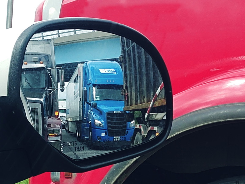 Photo of an automobile mirror with semi trucks in view