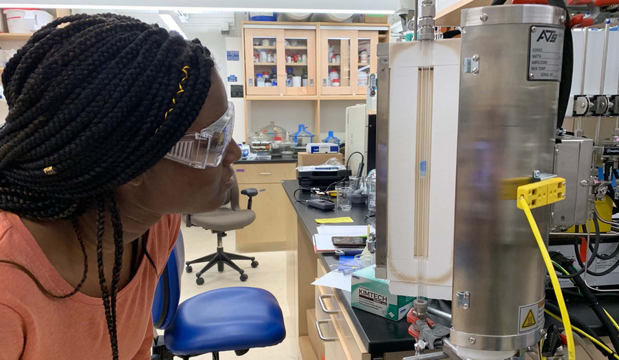 Photo of an MIT undergraduate student looking at a tabletop machine inside an engineering lab