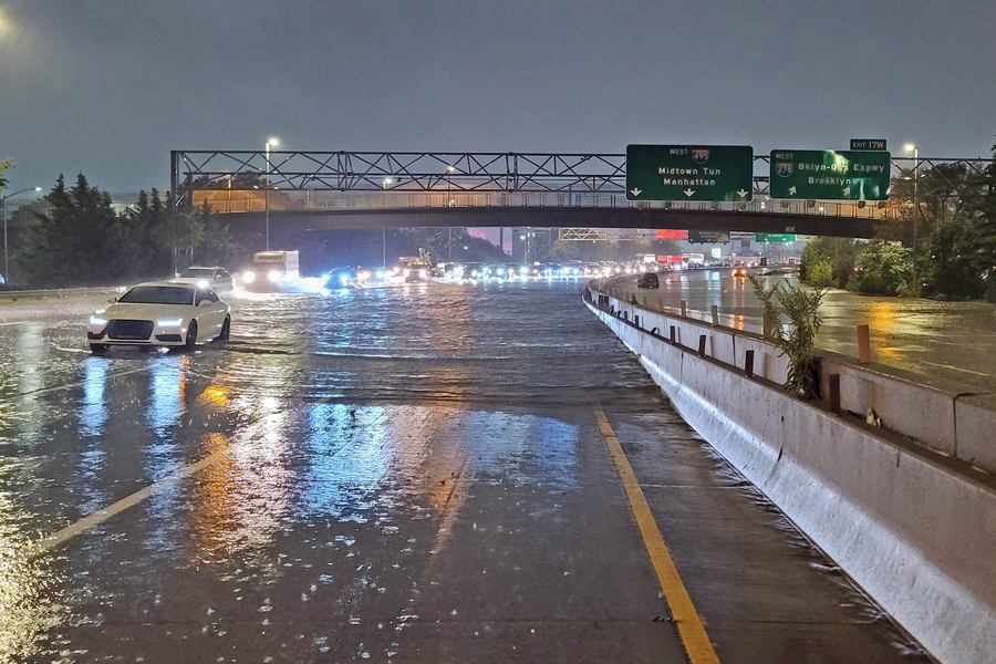 A flooded highway with a line of traffic driving through the water toward the camera