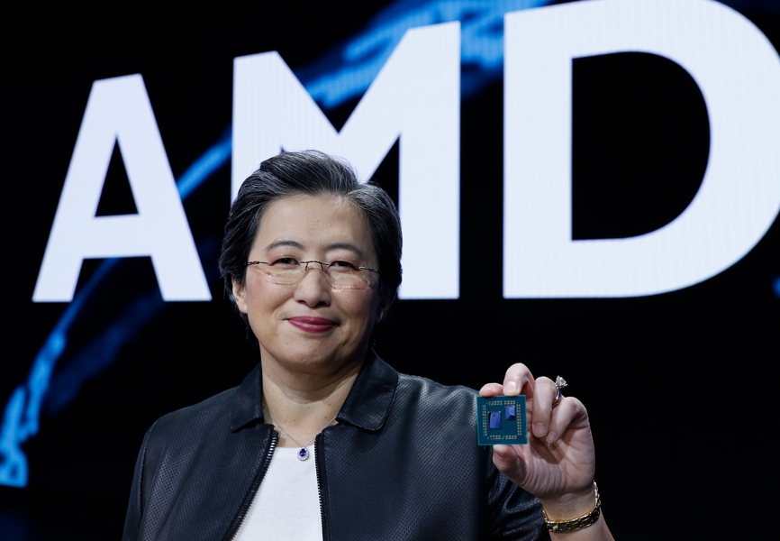 Photo of Lisa Su holding up a chip in front of a large A-M-D sign.