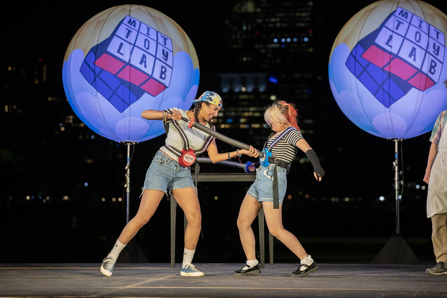 Photo of two students on stage, play-fencing with foam swords.