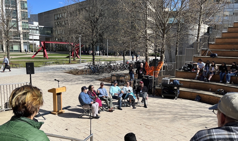 Photo of six people seated next to a podium at the base of MIT's outdoor amphitheater. Hockfield Court appears with with buildings and labs in the background.
