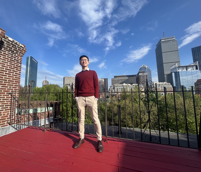 Photo of Chih-Wei Joshua Liu standing on a rooftop with the Boston skyline in background.