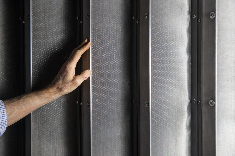 Photo of a man's hand touching turning vanes inside wind tunnel. Aluminum honeycomb filters are visible.