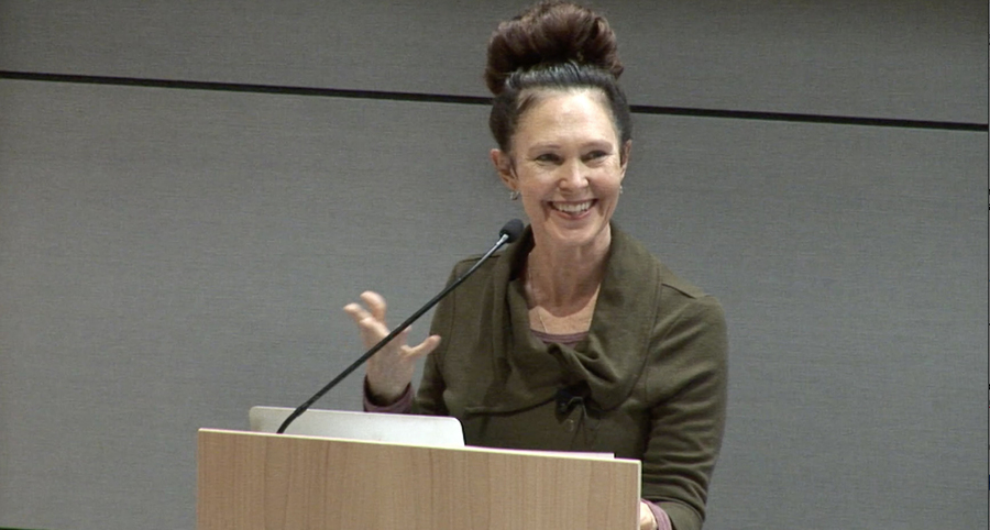 Screenshot of Willa Blythe Baker standing at a podium gesturing with her hand.