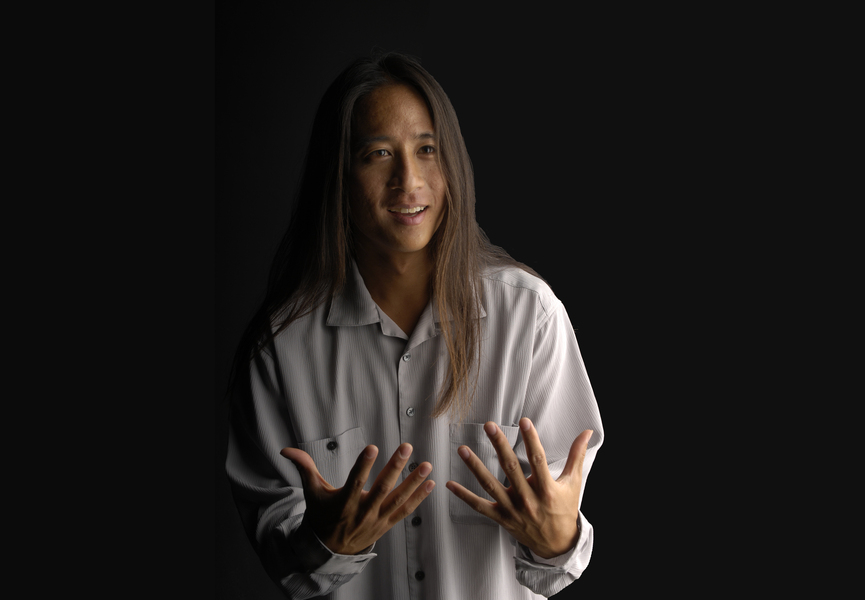 Photo of Kealoha Wong standing with his hands out in front of a black background 