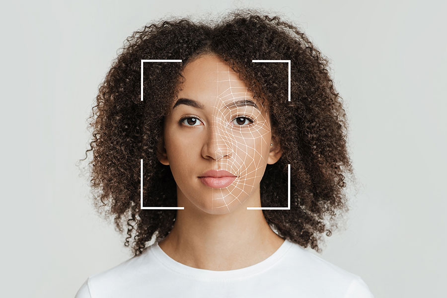 Photo of a woman in front of a white background with a cropped square outline focused on her face and small triangles marking the contours of her skin, indicating she is being scanned by a camera