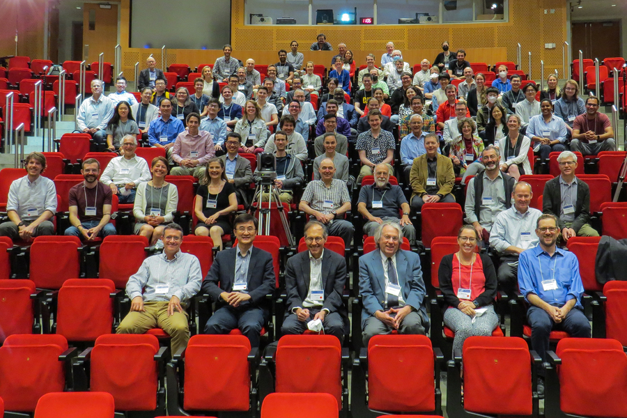 A lecture hall auditorium filled with roughly 60-70 people all smiling at the camera. Most of the seats are taken.