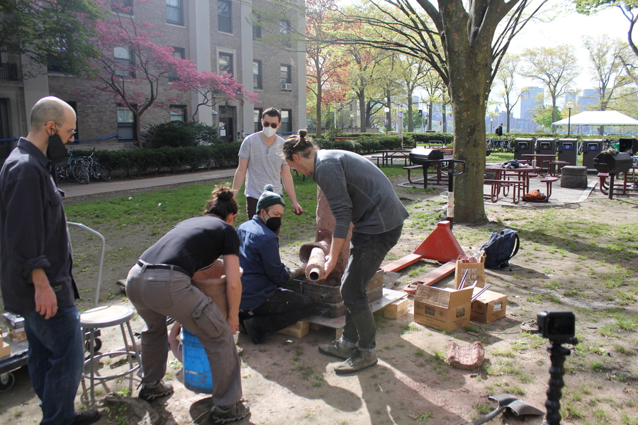 Photo of MIT students and instructors assembling a smelting furnace in a grassy courtyard.