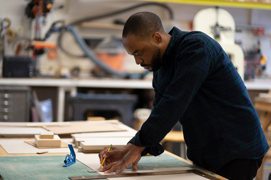 Photo of Justin Brazier at a workshop bench, holding a pencil against a straightedge ruler