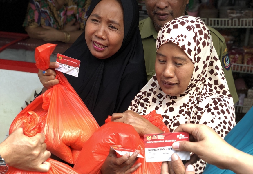 Photo of two women presenting ID cards to receive large orange bags of rice