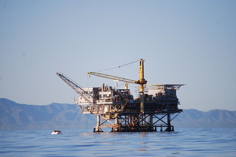 Photo of an oil rig in water, with low mountains in the background