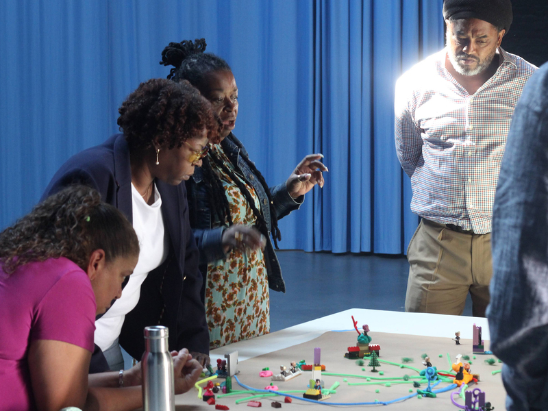 Photo of four people standing over a table with Lego-like models on it