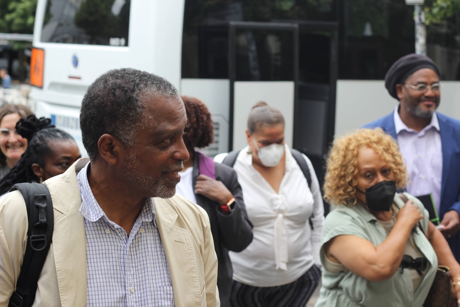 Photo of Phil Thompson leading a small group of people down a sidewalk, in front of a bus.