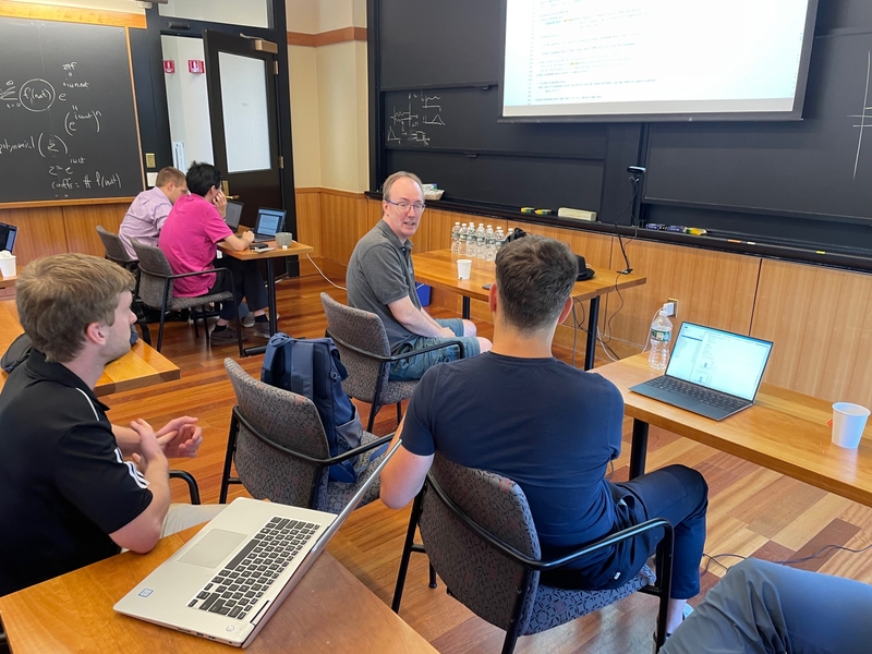 Photo of five men sitting at desks in a classroom.