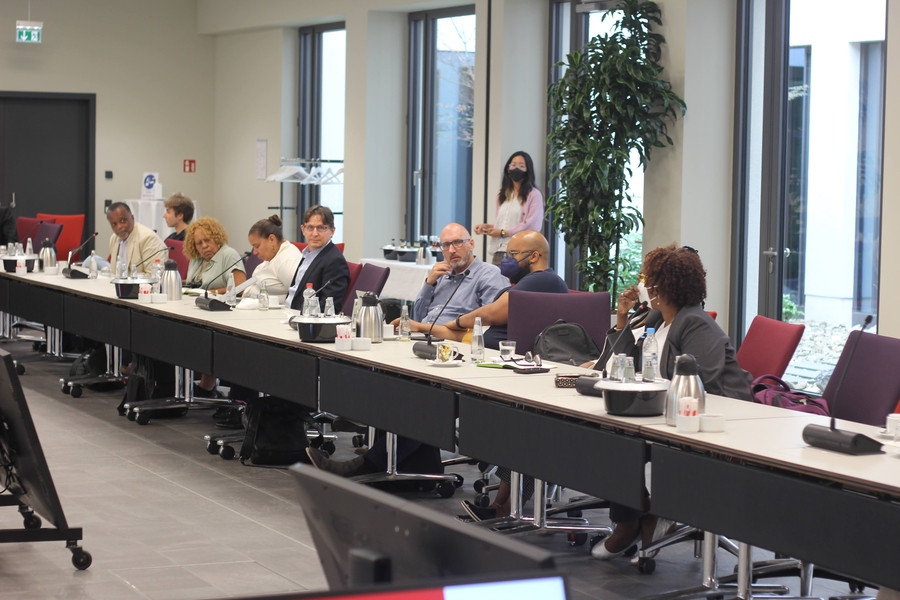 Photo of seven people sitting at a long table with laptops and microphones