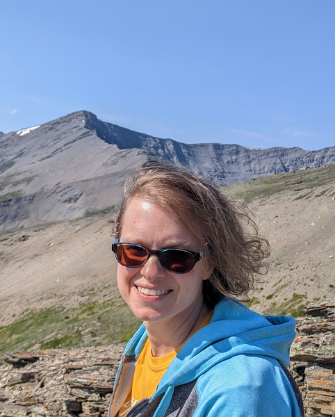 Headshot of Thea Keith-Lucas as she stands near a mountain ridge