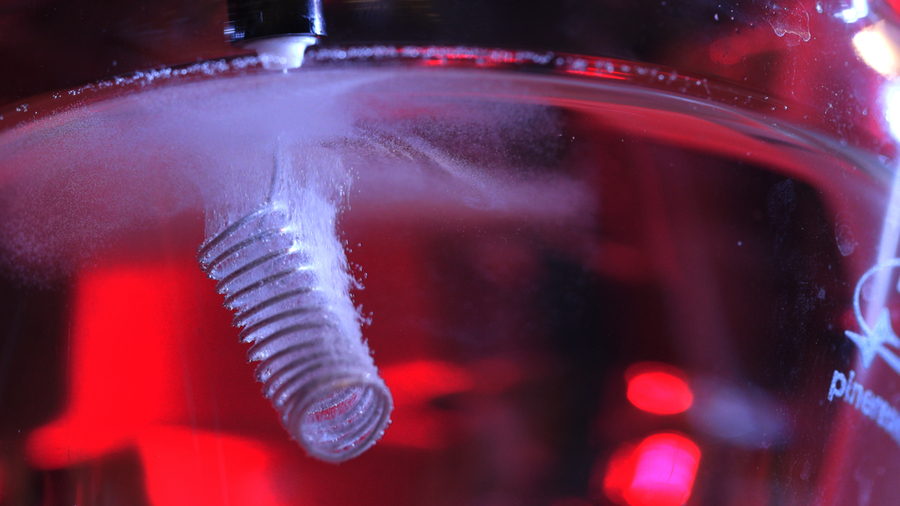 Close-up photo of a metal coil submerged in red-lit water generating bubbles