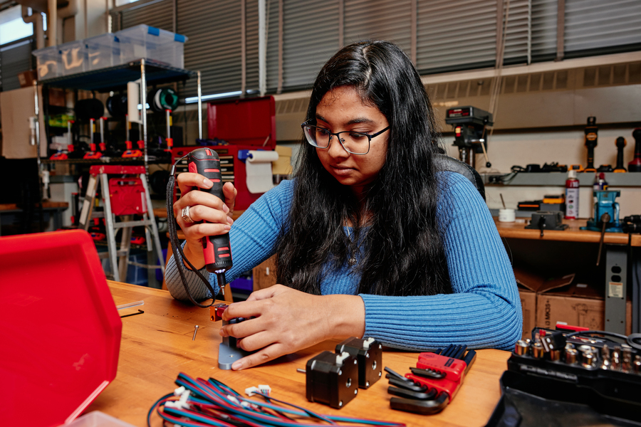 Aviva Jesse Levi holds a power tool over a partially built extrusion device in a workshop