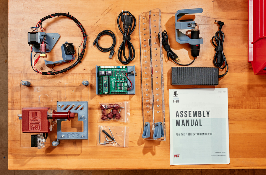 A view looking down at a table presentation of the parts for building an extrusion device, as well as the user manual with instructions on how to do so.