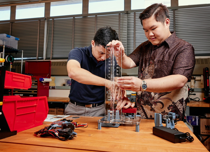 Russel Bradley works with Tanach Rojrungsasithorn at a benchtop work station to assemble a FrED device.
