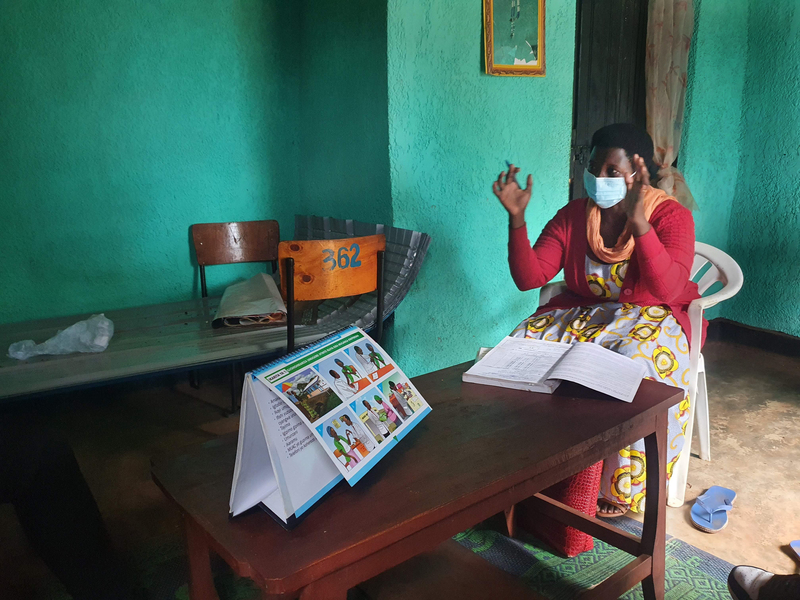Photo of a masked woman sitting at table in a brightly painted room