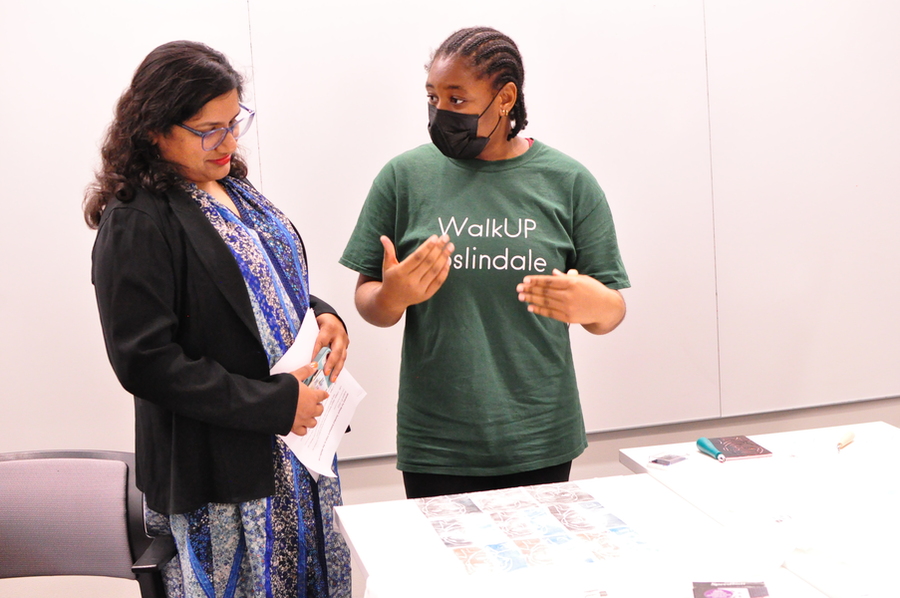 Sumbul Siddiqui looks at a T-shirt on a table while a student from Cambridge Rindge and Latin School talks about it.