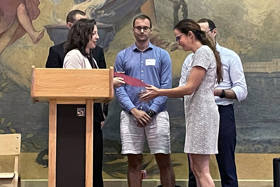 Muriel Medard receives an award at a podium, with several people looking on