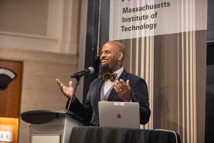 Daniels speaks at the podium, with MIT banner of a column behind him.