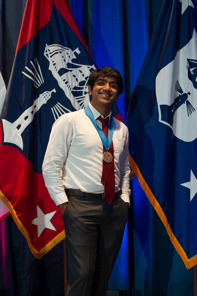 Vishnu Jayaprakash stands with a gold medal around his neck in front of two flags