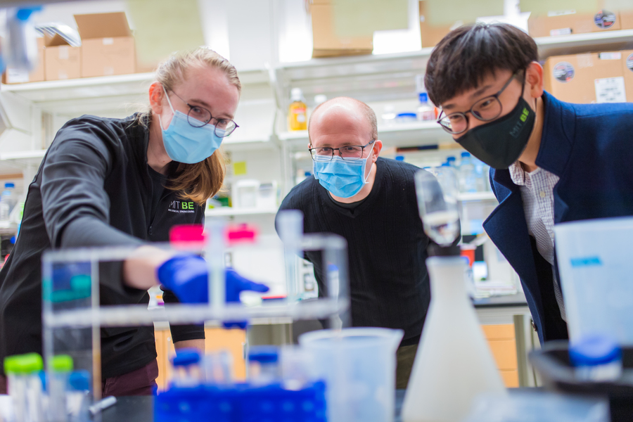 Michael Birnbaum and two students, wearing face masks and leaning over a lab workbench while one of the students points at something in the foreground