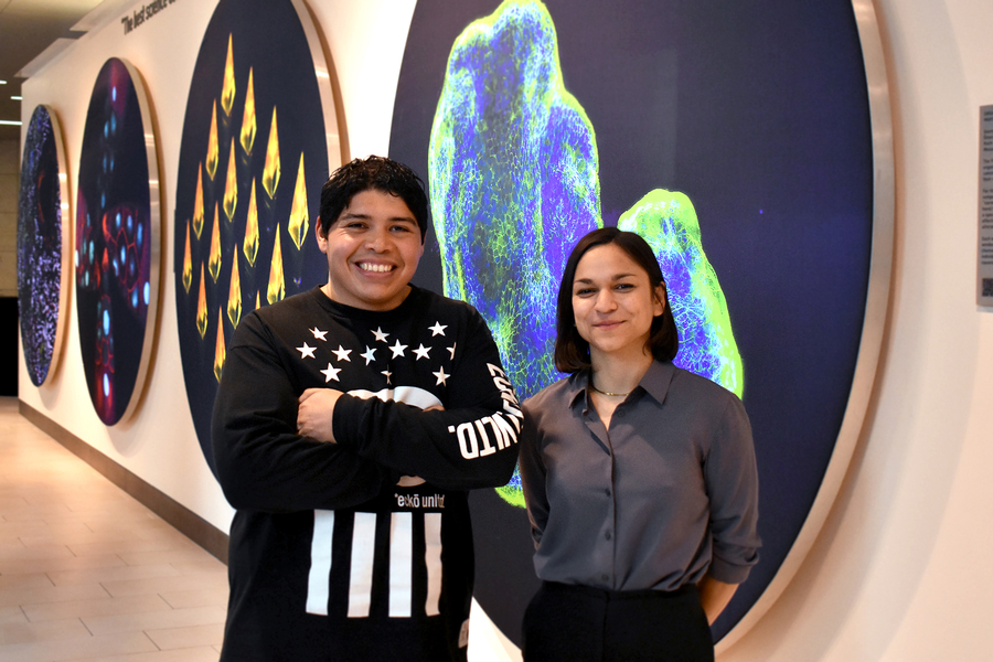 Alejandro Aguilera Castrejón and Melanie de Almeida stand together, in front of a long row of large, colorful scientific images
