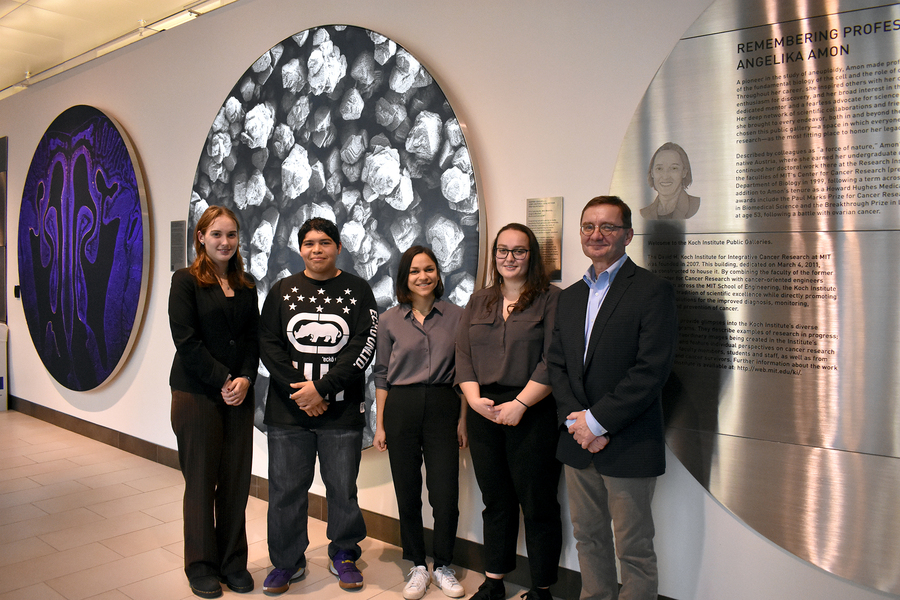 Five people stand next to a scientific photo exhibit with the title "Remembering Professor Angelika Amon”